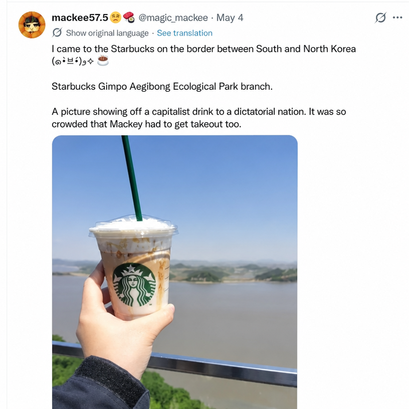 A screenshot of a Japanese tweet featuring a person holding a Starbucks cup on an outdoor railing, overlooking North Korean land across the river.