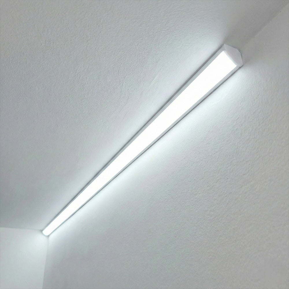 A long bar-shaped light fixture mounted where a white wall meets the ceiling emitting a cool white light