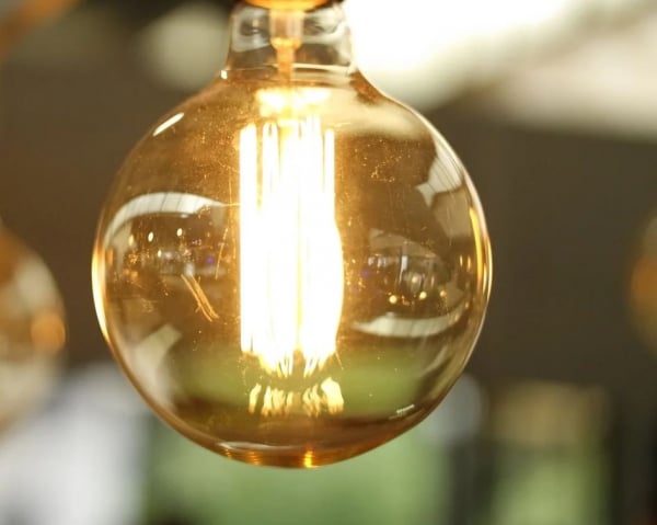 黄色い光を放つフィラメントが透けて見える丸い白熱電球の接写
