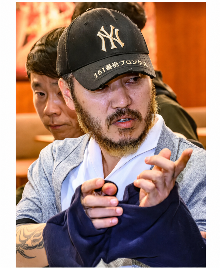 帽子を深くかぶり、髭を生やしたまま手振りで話す朴王烈の姿