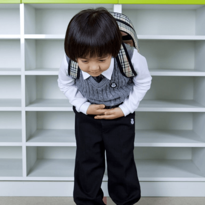 A young child in a kindergarten uniform bowing politely with both hands placed on their belly.