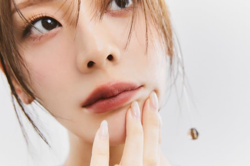 A close-up of a female model's face with her hand on her chin