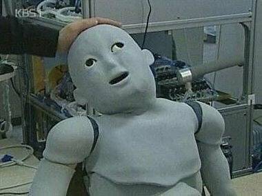 A grey humanoid robot with a dazed, vacant expression and its mouth hanging open, being touched by someone.