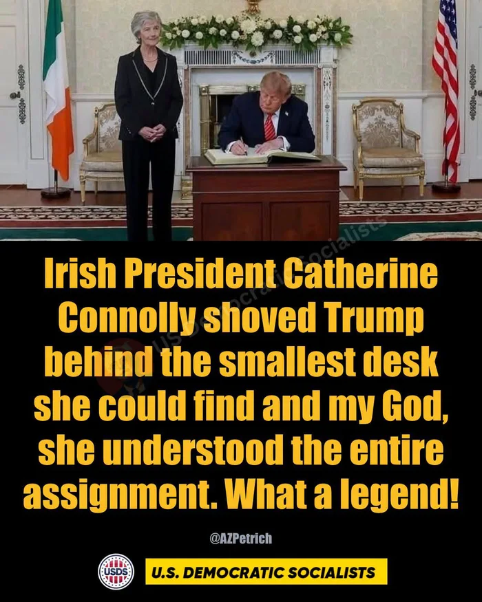Donald Trump seated writing in a guestbook at an unusually small desk while Catherine Connolly stands beside him