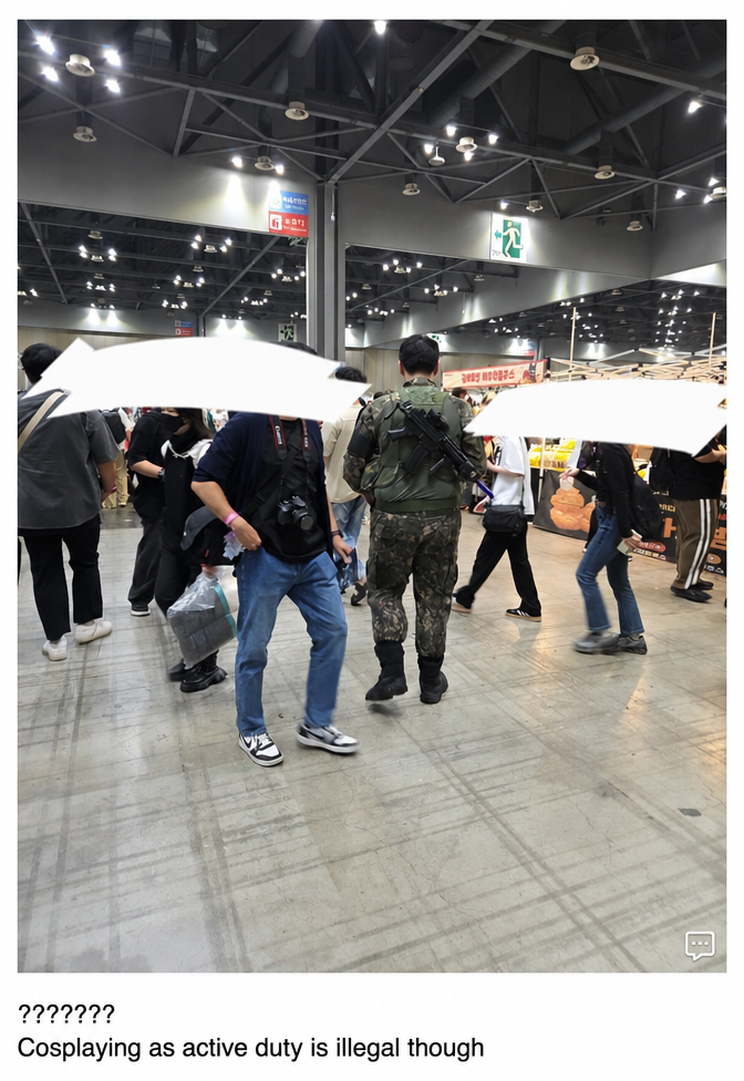 A rear view of a person walking inside an event venue wearing a military uniform and carrying a model firearm.