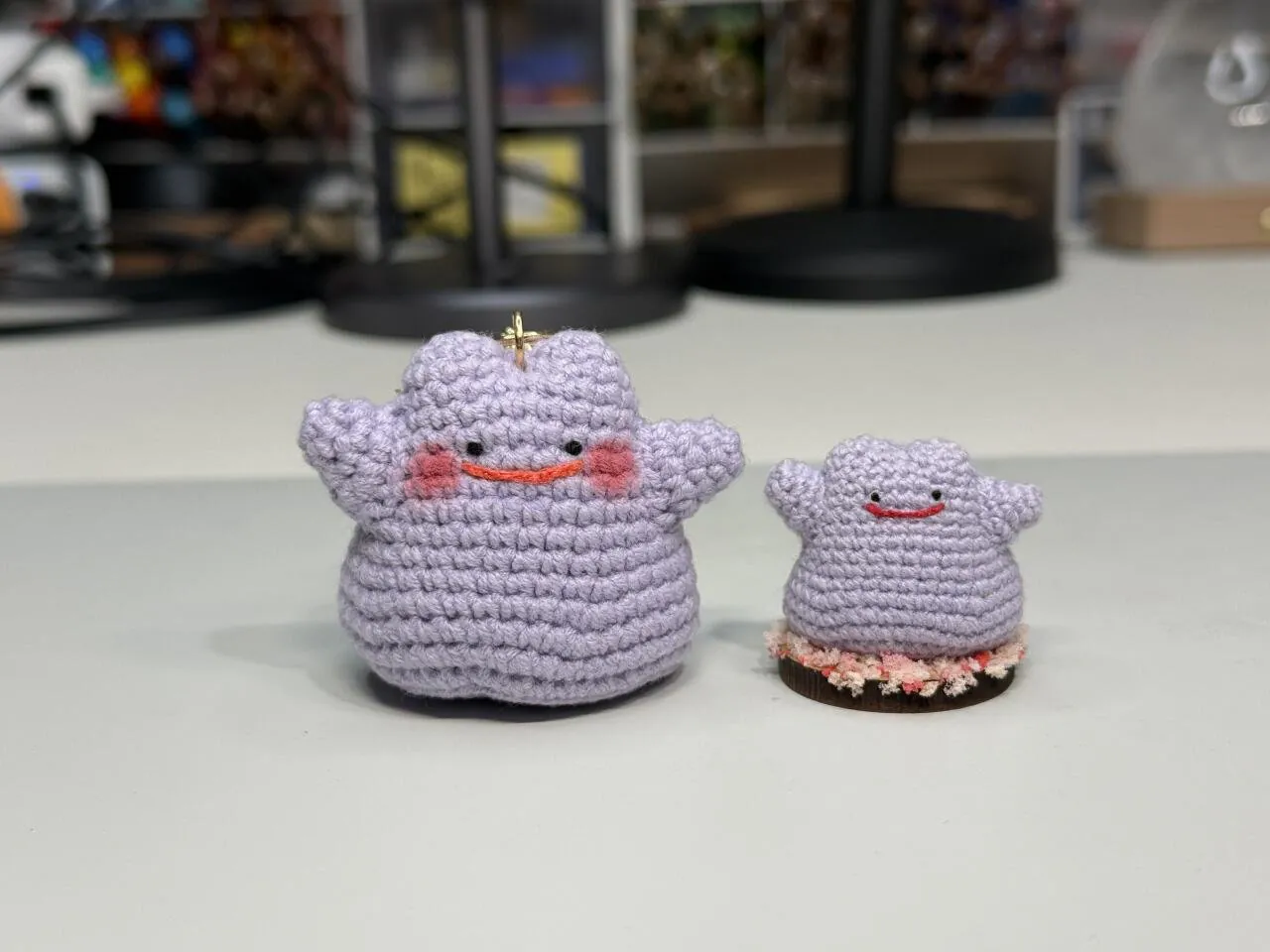 Two finished purple Ditto crochet dolls. The one on the left is for a key ring with red blush marks, and the one on the right sits on a flower-shaped base as a mini desk doll.