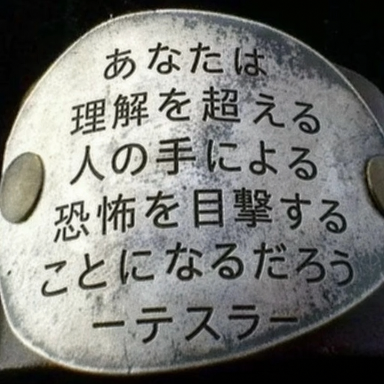 「YOU WILL LIVE TO SEE MAN-MADE HORRORS BEYOND YOUR COMPREHENSION -Tesla-（お前は理解を超えた人工的な恐怖を目の当たりにするだろう -テスラ-）」と刻印された金属プレートのアップ。