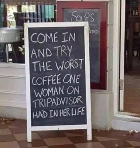 A sidewalk chalkboard sign outside a cafe reading: 'Come in and try the worst coffee one woman on TripAdvisor had in her life.'