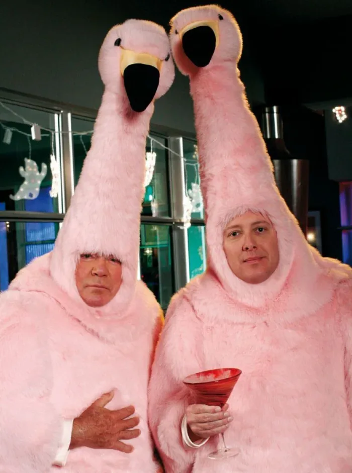 William Shatner and James Spader dressed in oversized pink flamingo suits, with Spader holding a cocktail.