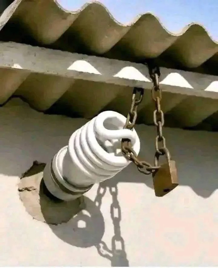 A spiral CFL light bulb mounted on an exterior wall secured tightly with a metal chain and padlock.