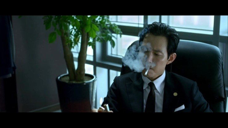 映画『新しき世界』でスーツを着て椅子に座り、タバコを吸っているイ・ジャソン（イ・ジョンジェ）
