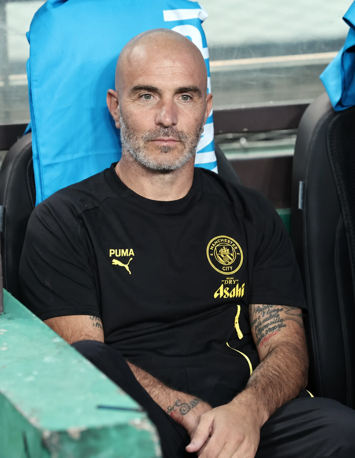 Enzo Maresca, who bears a resemblance to Pep Guardiola, sitting while wearing a Manchester City uniform