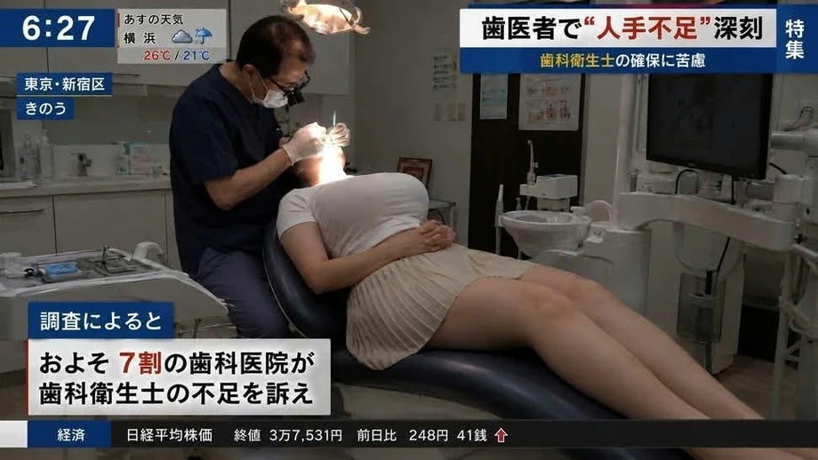 歯科の人手不足を報じる日本のニュース番組のキャプチャ。診察台に横たわる胸元の強調された女性患者と治療を行う歯科医。