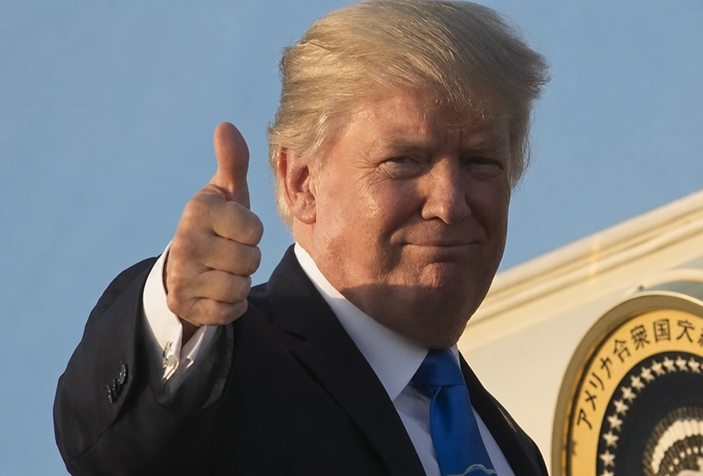 大統領紋章を背景にサムズアップしながら微笑むドナルド・トランプ