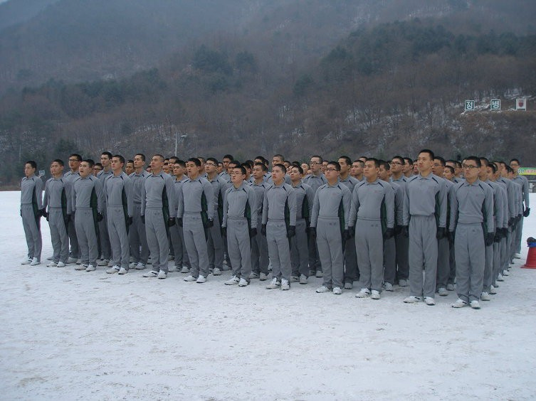 Recruits standing in formation on a snow-covered drill ground wearing gray physical training uniforms