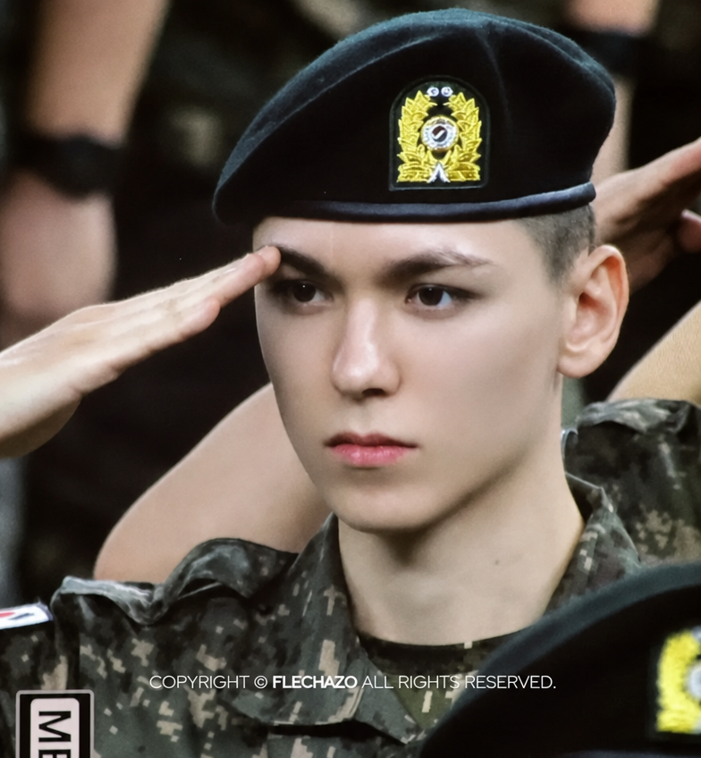 Close-up of SEVENTEEN's Vernon in a beret saluting with sharp posture.