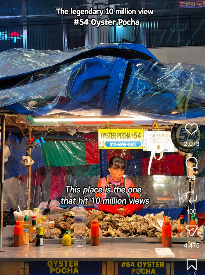 A short-form video screenshot showing a mountain of oysters piled up on a street stall counter, with a vendor standing by.