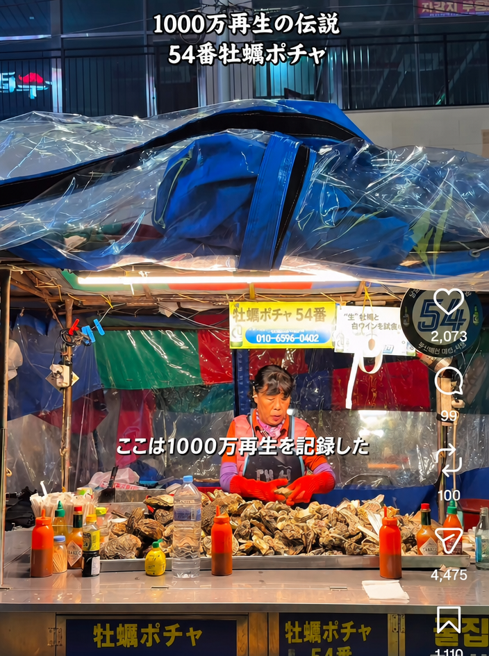 露店の屋台カウンターに牡蠣が山のように積まれており、店主が立っているショート動画のスクリーンショット。