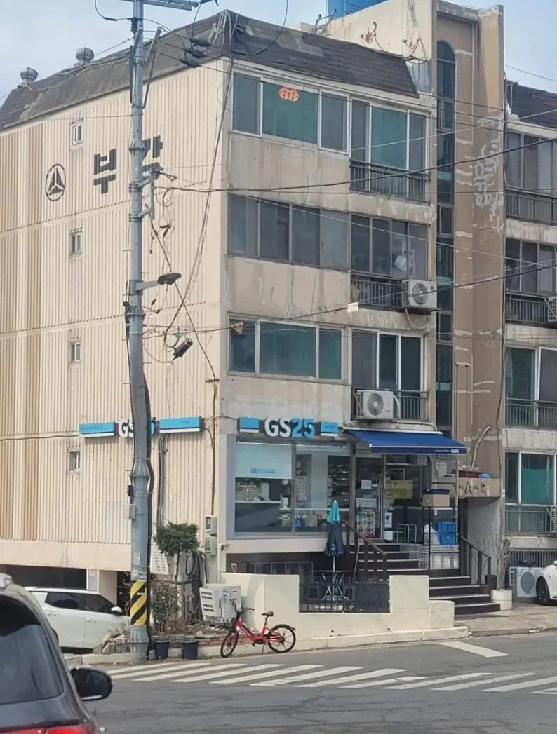 A ground-floor residential unit of an old multi-family villa converted into an operating GS25 convenience store with large glass windows and dedicated stairs.