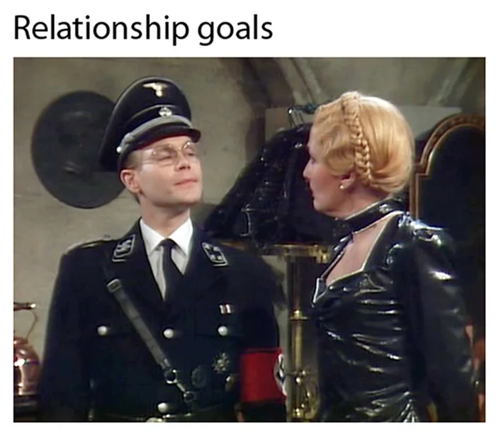 イギリスのシットコム『アロ・アロ（'Allo 'Allo!）』のヘル・フリックとヘルガが、制服と革の衣装で一緒に立っている。
