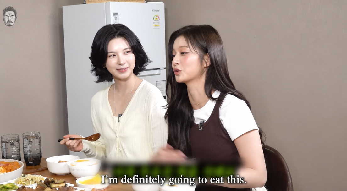 NMIXX's Sullyoon and Bae chatting in front of tteokbokki on a YouTube broadcast