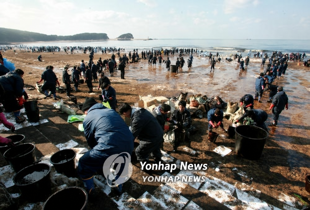 Volunteers lining up on a wide sandy beach, using bowls and buckets to scoop up and wipe away oil residue.