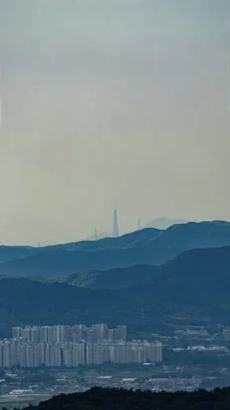 遠くの山並みの向こうにかすかにシルエットを見せるロッテワールドタワーの全景。