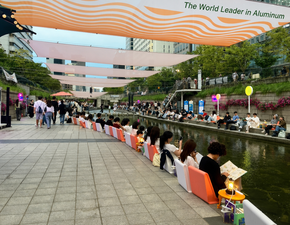 Citizens sitting in a row by the Cheonggyecheon stream, each reading a book.