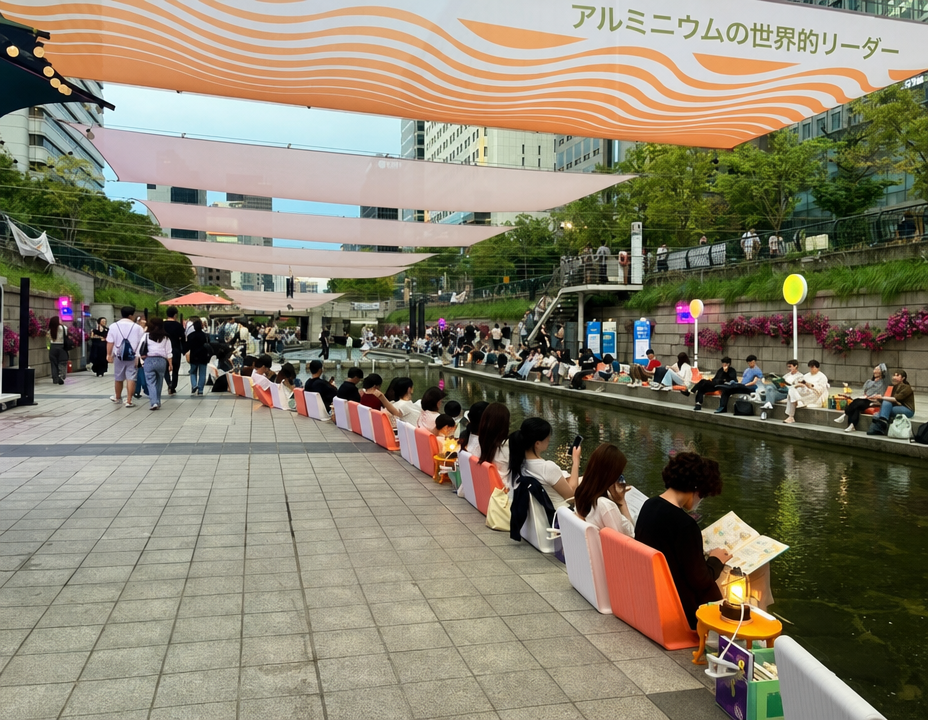 清渓川の水辺に並んで座り、それぞれ本を読んでいる市民たちの姿。