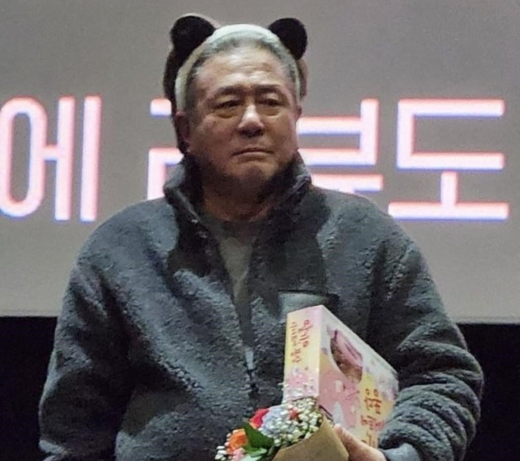 Actor Choi Min-sik wearing a bear ear headband while holding a bouquet of flowers and gifts