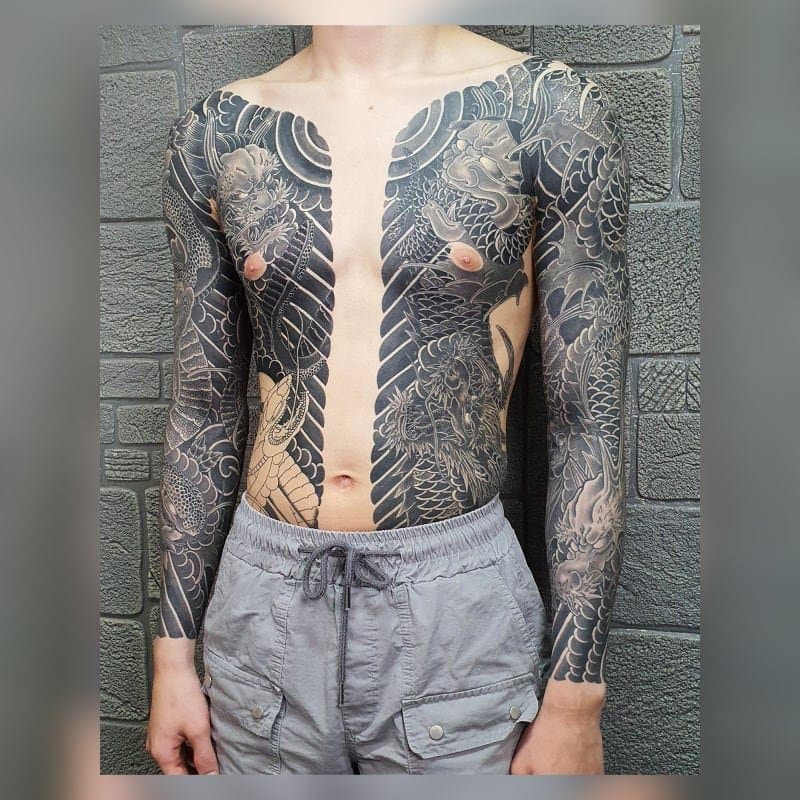 A man whose upper body is covered in black-and-grey irezumi tattoos, leaving circular bare patches around both nipples.