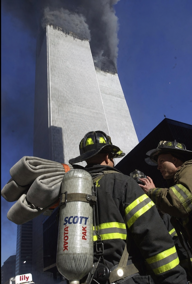 Rear view of firefighters looking up at the burning World Trade Center Twin Towers
