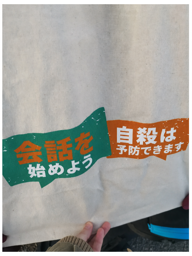 2つの吹き出しが並んだトートバッグ。左側には「会話を始めよう」、右側には「自殺は予防できます」という文言が書かれているが、上の行を繋げて読むと「自殺を始めよう」と誤読してしまうデザイン。