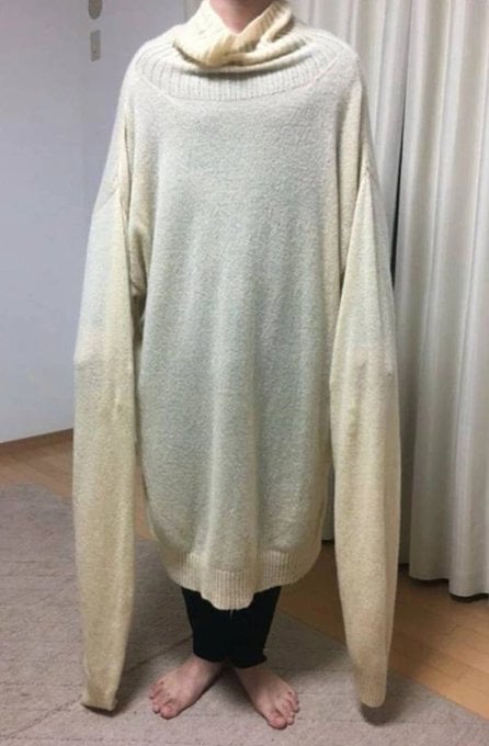 A photo of someone wearing the abnormally stretched white turtleneck knit sweater, with both sleeves hanging all the way down near their ankles.