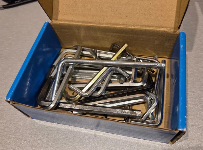 様々な金属製の六角レンチとヘックスレンチが縁まで詰まった小さな段ボール箱。