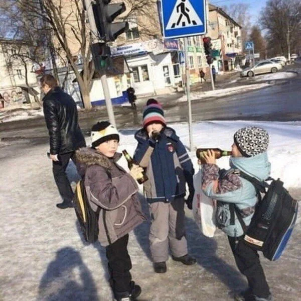 Young schoolkids in winter coats and backpacks drinking from glass beer bottles on a street corner