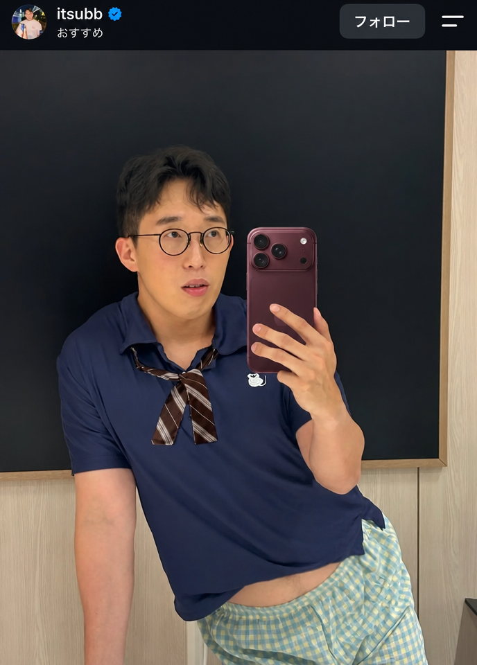YouTuberのITSUBBがチェック柄のショートパンツにリボンタイをつけて鏡越しに自撮りをし、腰を少し見せている様子