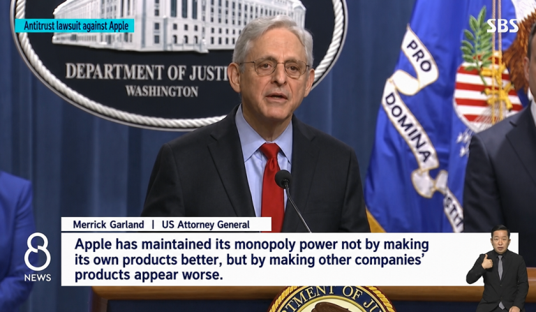 A news screen capture of US Attorney General Merrick Garland speaking at a press conference regarding the Apple antitrust lawsuit.
