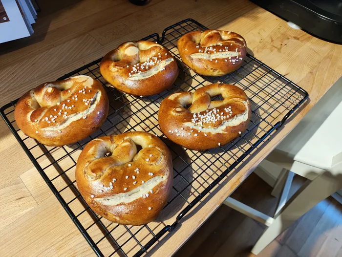 Five freshly baked German pretzels cooling on a wire rack on a wooden countertop.