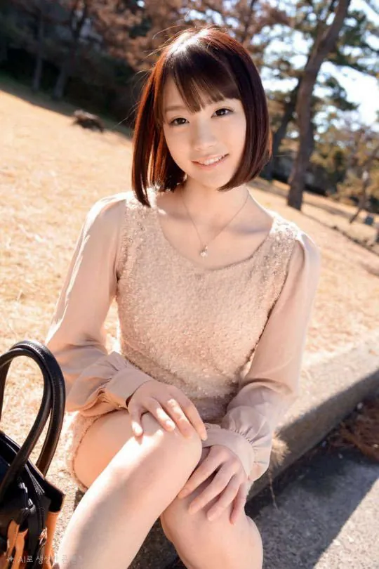 Airi Suzumura with short hair, wearing a beige dress, smiling while sitting on a roadside curb