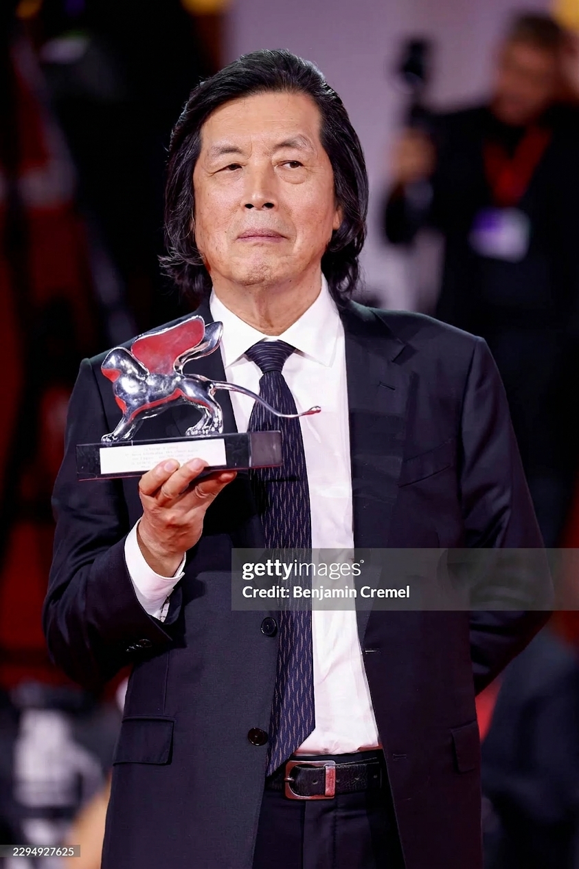 Director Lee Chang-dong looking directly at the camera while holding the Venice Film Festival Silver Lion trophy.