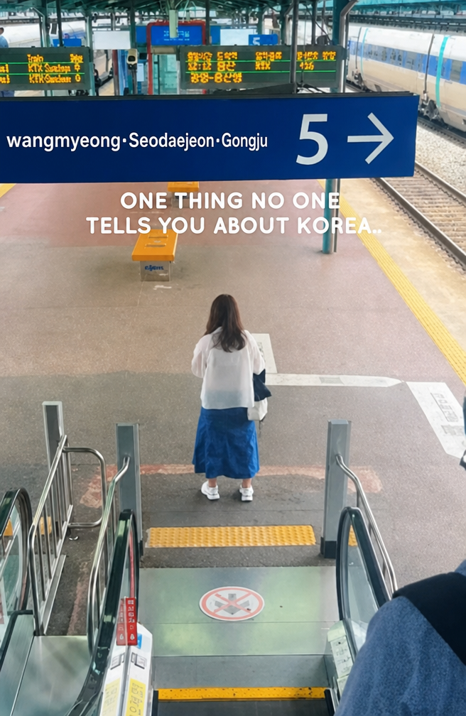 The back of a passenger standing still in the middle of the hallway right in front of the exit, immediately after coming down the train station escalator.