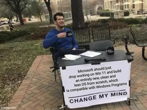 Steven Crowder Change My Mind meme with a sign reading 'Microsoft should just drop working on Win 11 and build an entirely new, clean and lean OS from scratch, which is compatible with Windows Programs. CHANGE MY MIND.'