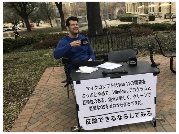スティーブン・クラウダーの「Change My Mind」ミーム。看板には「マイクロソフトはWin 11の開発をさっさとやめて、Windowsプログラムと互換性のある、完全に新しく、クリーンで軽量なOSをゼロから作るべきだ。反論できるならしてみろ。」と書かれている。