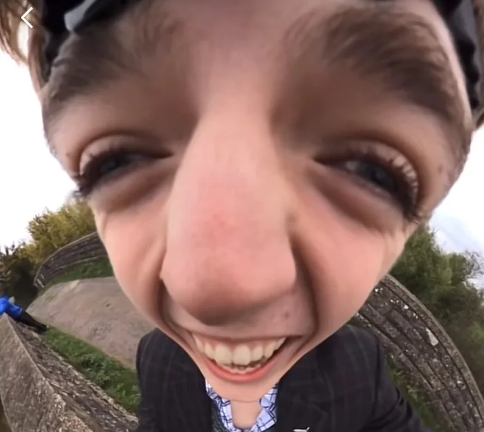 Distorted wide-angle close-up of a young man wearing a suit smiling widely directly into the camera lens outdoors