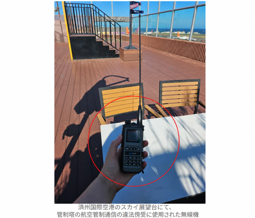 空港の屋外展望台で、長いアンテナが付いた黒い無線機を手に持っている様子。