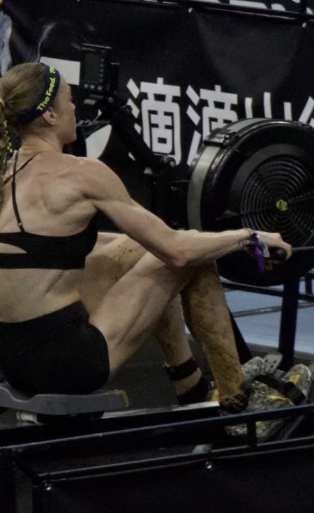 Side view of a female athlete performing rowing machine exercises with excrement visible on her legs during an indoor fitness race.