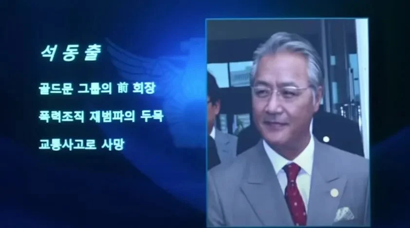 Screenshot of a news broadcast announcing the death of Chairman Seok Dong-chool of Goldmoon Group from the movie 'New World'