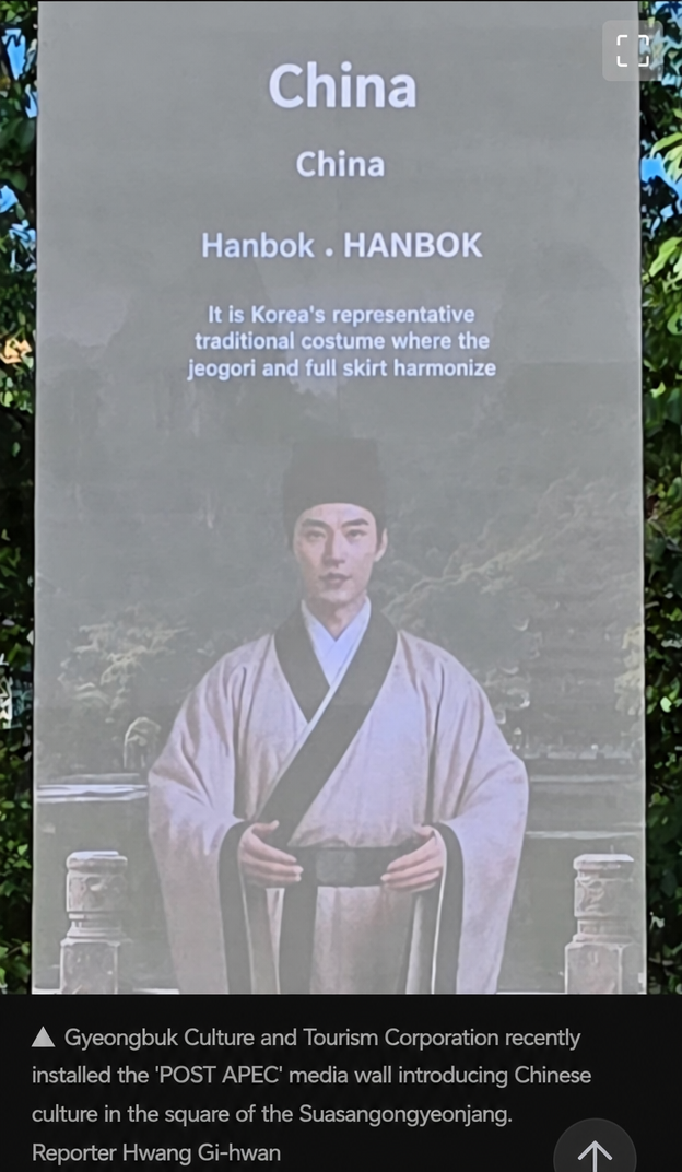 Outdoor media wall screen. Top shows 'China', below it 'Hanbok HANBOK' and an explanation of Korea's representative traditional clothing. In the background, a man in Chinese-style clothing is standing.