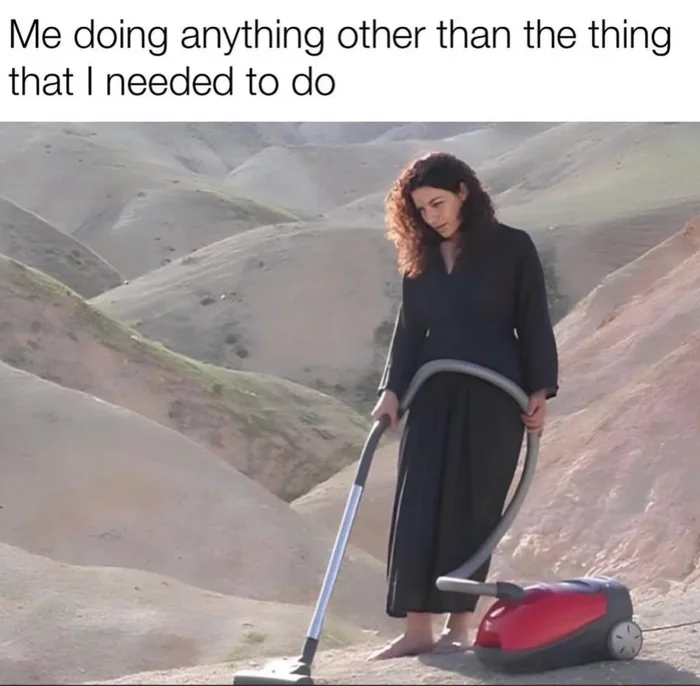 A woman in a black dress vacuums a dirt hill in a barren landscape.